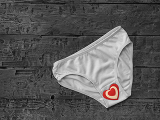 Black and white image of women's panties and red heart on wooden background. Flat lay.
