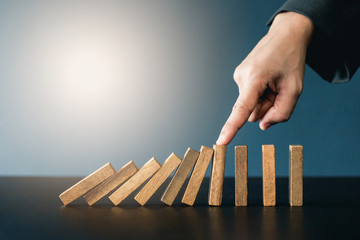 Close up of businessgirl hand Stopping Falling wooden Dominoes effect from continuous toppled or...