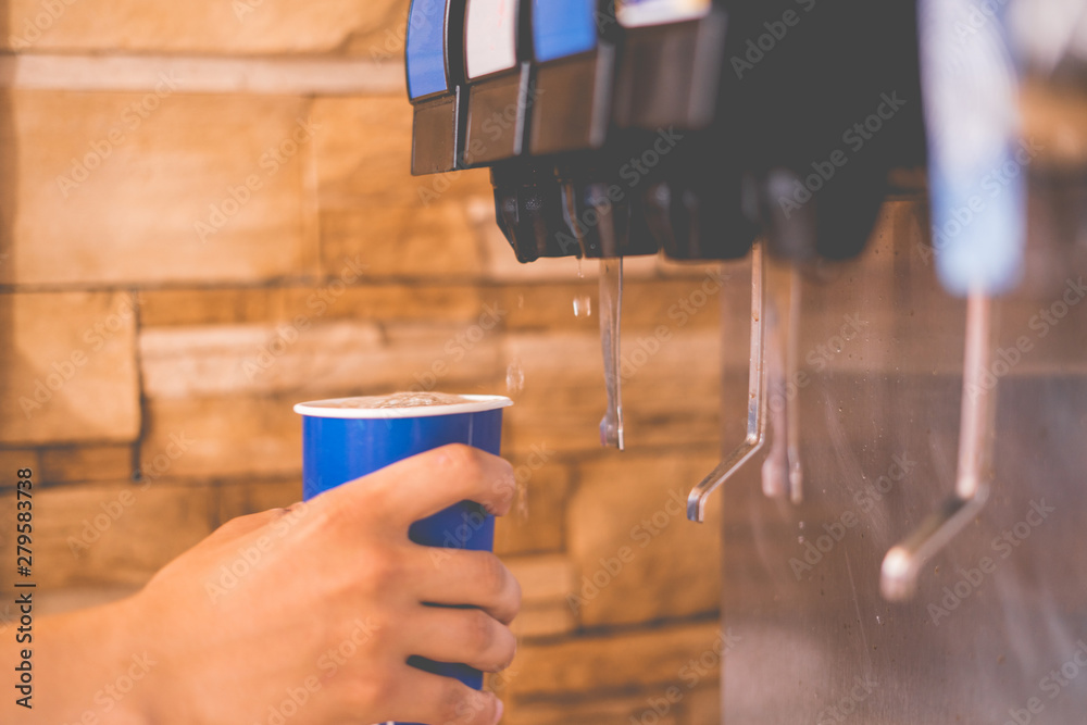 Wall mural hand holding a paper glass to pour the lemonade soda soft drink  machine  in a fastfood restaurant