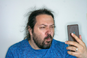 Middle-aged untidy man peers at the screen of a mobile phone to see small text
