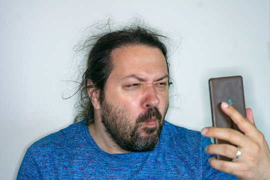 Middle-aged untidy man peers at the screen of a mobile phone to see small text