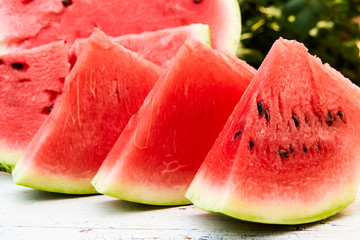 Fresh ripe striped sliced watermelon on a wooden old table, against the background of green leaves, outdoors.