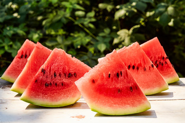 Fresh ripe striped sliced watermelon on a wooden old table, against the background of green leaves, outdoors.