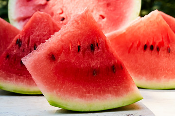 Fresh ripe striped sliced watermelon on a wooden old table, against the background of green leaves, outdoors.