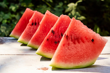 Fresh ripe striped sliced watermelon on a wooden old table, against the background of green leaves, outdoors.