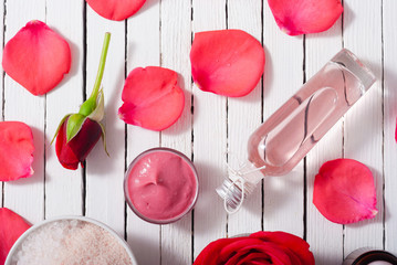 perfume, body care and beauty products with red roses, pink petals on white wood table