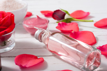 perfume, body care and beauty products with red roses, pink petals on white wood table