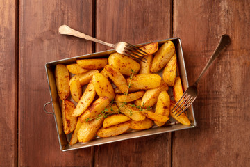 Potato wedges, oven baked with thyme, top shot on a baking sheet on a dark rustic wooden background