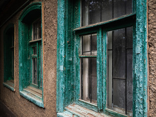 The old wooden Windows are green. Gray building with dirty, scratched Windows