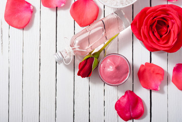 perfume, body care and beauty products with red roses, pink petals on white wood table