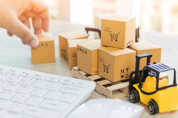 Mini forklift truck load cardboard boxes with symbols on wood pallet and fingers touch box and keyboard nearby. Logistics and transportation management ideas and Industry business commercial concept. - obrazy, fototapety, plakaty