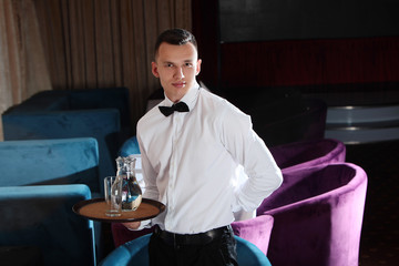 A young, handsome waiter is holding a tray in a carafe of water. The concept of the restaurant business. The staff in the field of restaurant business.