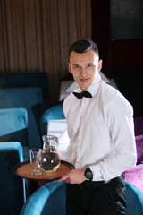 A young, handsome waiter is holding a tray in a carafe of water. The concept of the restaurant business. The staff in the field of restaurant business.