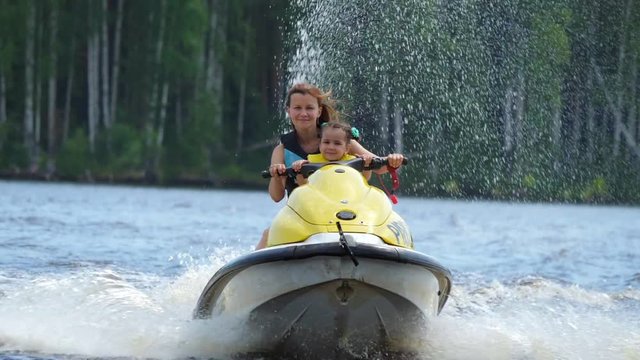 Mom and daughter ride along the river on a personal watercraft and have fun. Sunny summer day. Slow motion.