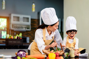 Happy asian family in the kitchen.Mother and son help to make vegetable salad.Mom teaching kid boy cooking healthy salad for dinner.