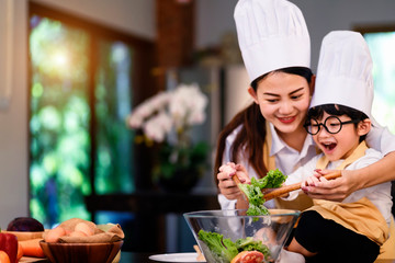 Happy asian family in the kitchen.Mother and son help to make vegetable salad.Mom teaching kid boy cooking healthy salad for dinner.
