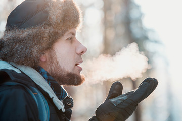 Man breathing on gloves in winter forest