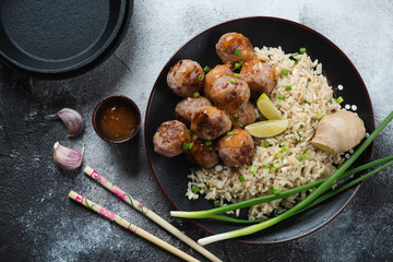 Black plate with roasted pork meatballs and rice, flatlay over grey stone background