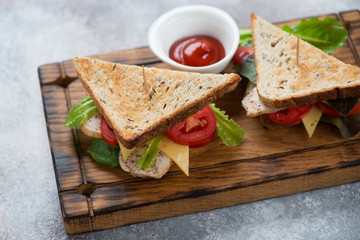 Sandwiches with grain bread, chicken fillet, cheese and vegetables on a rustic wooden serving board