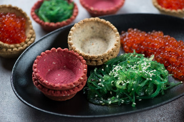 Closeup of vegetable tartlets with seaweed salad and red caviar, studio shot
