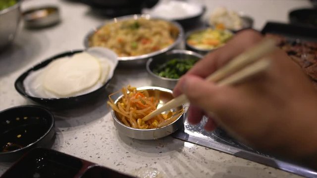 This slow motion POV video shows chopsticks grabbing banchan korean bbq food and moving it towards the viewers mouth to eat.