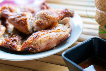 Chicken marinated with spices then grilled until cooked. Chopped into pieces, placed on a plate on a bamboo table with a medium spicy sauce.