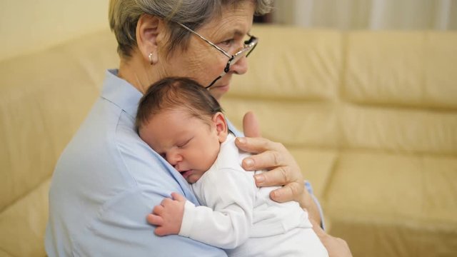 Old grandmother with gray hair and eyeglasses holding very young newborn child