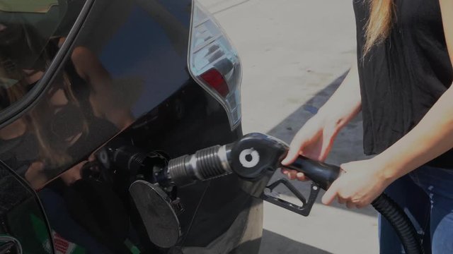 This video shows a woman opening her gas cap and pumping gas into a car at a gas station.