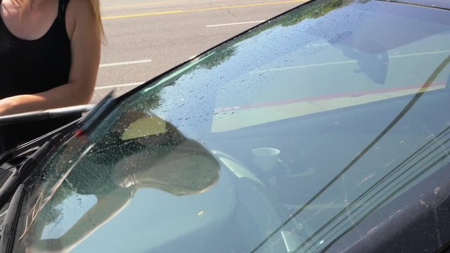 This video shows a woman washing her car windshield window with gas station squeegee on a sunny day.
