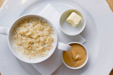 Oatmeal porridge, peanut paste, butter, napkin in white plate on table. Breakfast concept. Close-up, copy space, top view