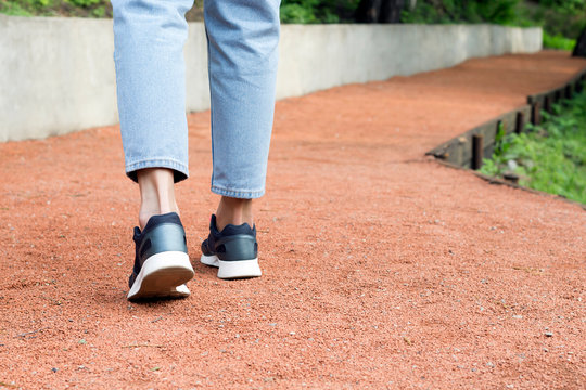Woman's legs walking on red gravel road in summer park. Outdoor sport, walking concept. Close-up, copy space