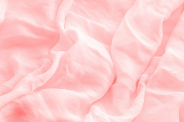 Obraz premium Textured background from light cotton natural fabric. Waves from the folds of light linen of a pale pinkish-orange shade.