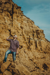 Naklejka premium brutal man in glasses and a hat on the background of rocks