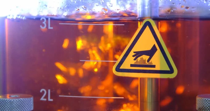 Chemical reaction in a flask with a liquid that is mixed. Close-up of the operation of the agitator in a red liquid with air blowing and the formation of bubbles. Hot surface warning sign.