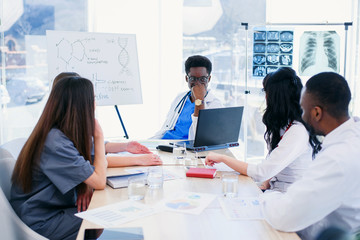 Multiracial group of professional medical doctors have a meeting at conference room in hospital. The team of young doctors discuss the results of analyzes and the history of patient's illness.