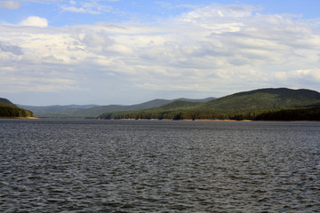 View of the Yenisei River and the rocky shore with trees lit by the sun.