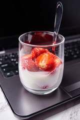 Glass of healthy yogurt with fresh sliced strawberry standing on laptop computer, copy space. Healthy breakfast, food concept