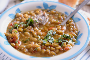 Mixed legumes and peas soup with meat and some greenary at a bowl, close up