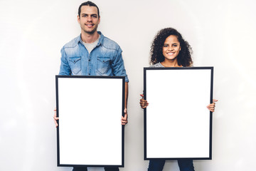 Two friends posing and showing empty white blank board with copy space for text or ad together on...