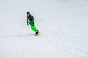Fototapeta na wymiar Unrecognizable snowboarder skiing in bright green suit, protective glasses mask on the slope, overalls. Winter sport, leisure outdoor lifestile