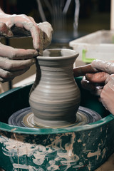 Man and woman hands pottery studying in studio. Creating vase. Hands in the clay and the potter's wheel with the product. Pottery class close up.