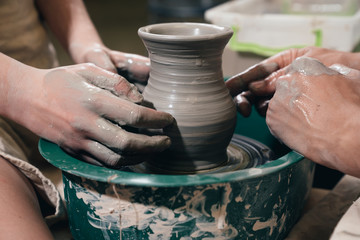 Fototapeta na wymiar Man and woman hands pottery studying in studio. Creating vase. Hands in the clay and the potter's wheel with the product. Pottery class close up.