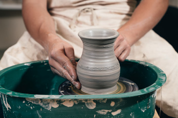 Young man making ceramic pot on the pottery wheel. Creating potter working on the wheel shaping clay making vase.