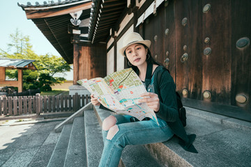 Obraz premium Young woman traveler with backpack and hat looking paper map in shitennoji temple osaka japan. Traveling asia in summer holidays. relaxed girl visitor in shrine sitting on rock stairs thinking way.