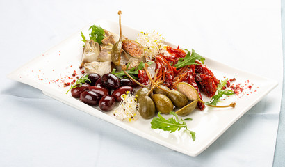 A plate of appetizers with Italian antipasti. Pickled anchovies, capers, mushrooms and sun-dried tomatoes. On light background