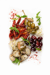 A plate of appetizers with Italian antipasti. Pickled anchovies, capers, mushrooms and sun-dried tomatoes. On light background