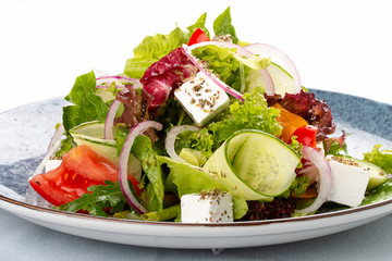 Classic Greek salad of tomatoes, cucumbers, red pepper, onions with olives, oregano and feta cheese. On a decorative plate