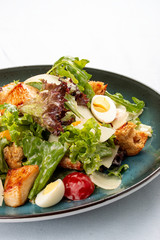Caesar Salad. Delicious salad with croutons, fried chicken breast, grated Parmesan cheese and lettuce, with sauce in a gravy boat. On a decorative plate