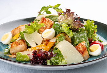 Caesar Salad. Delicious salad with croutons, fried chicken breast, grated Parmesan cheese and lettuce, with sauce in a gravy boat. On a decorative plate