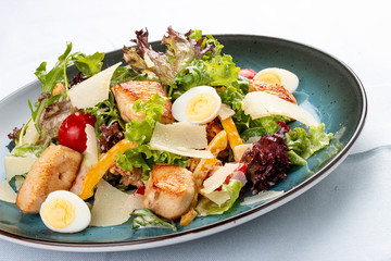 Caesar Salad. Delicious salad with croutons, fried chicken breast, grated Parmesan cheese and lettuce, with sauce in a gravy boat. On a decorative plate